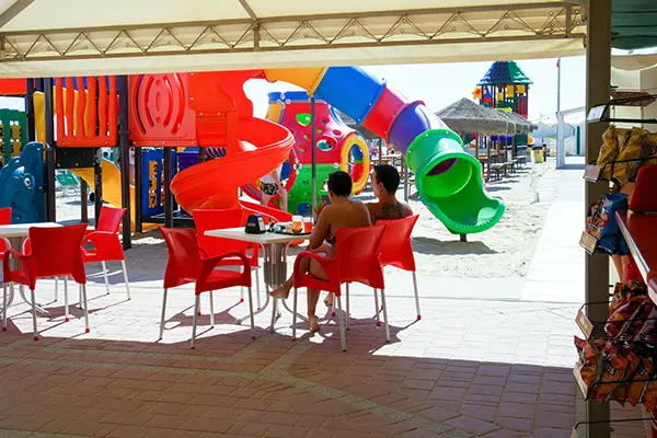 Due persone sedute ad un tavolino del bar sulla spiaggia, sullo sfondo giochi colorati per bambini